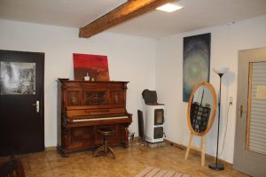 Ein Klavier steht im Musikraum, daneben ein Holzofen und ein großer, ovaler Spiegel