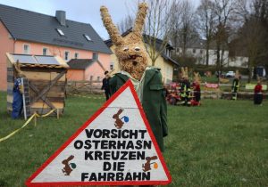 Osterhase in Polizeiuniform mit Hinweisschild "Vorsicht - Osterhasen kreuzen die Fahrbahn!"