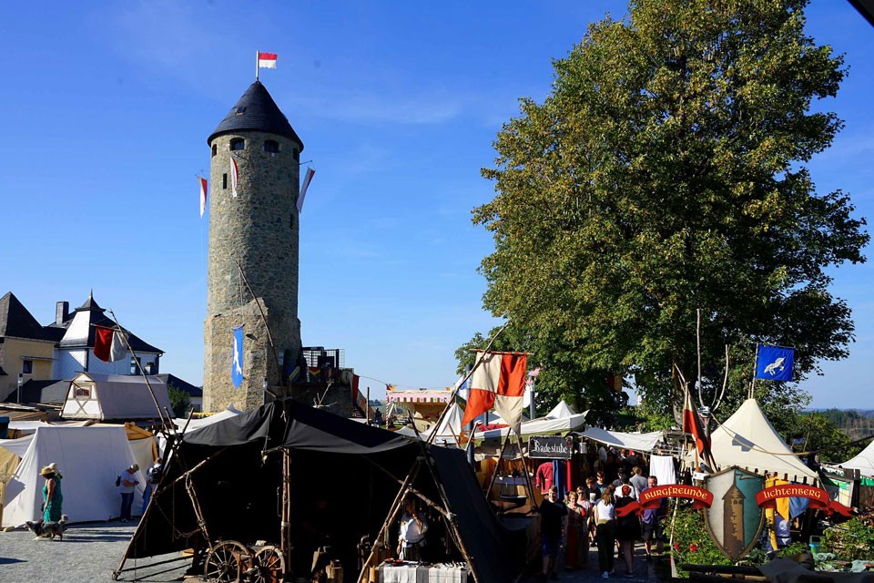 Das Foto zeigt rechts den Turm der Burgruine Lichtenberg. Davor und drum herum stehen Buden und Zelte im mittelalterlichen Stil.