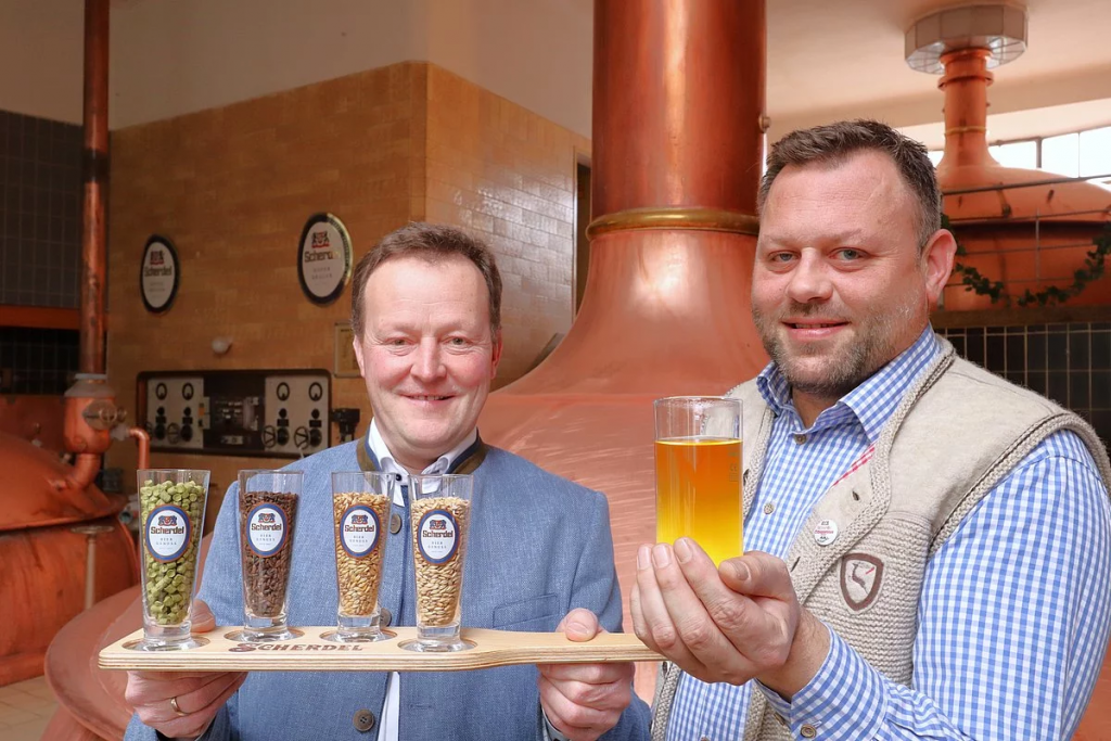 Das Foto zeigt links den Prokuristen Uwe Unverdorben mit den Bestandteilen des Bieres in Biergläsern auf einem Tablett. Rechts von ihm steht Braumeister Sascha Greßmann mit einem Glas Schlappenbier in der Hand.