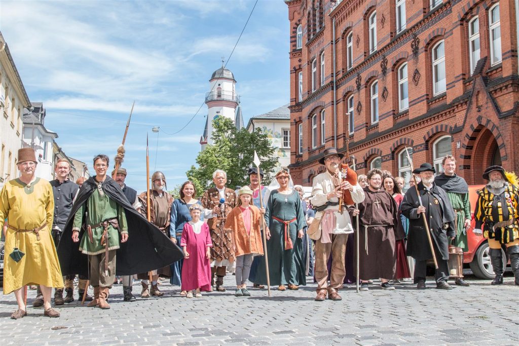 Das Foto zeigt eine Gruppe von Menschen in traditioneller Tracht, die durch die Klosterstraße laufen. Im Hintergrund ist der Turm des Rathauses zu sehen.