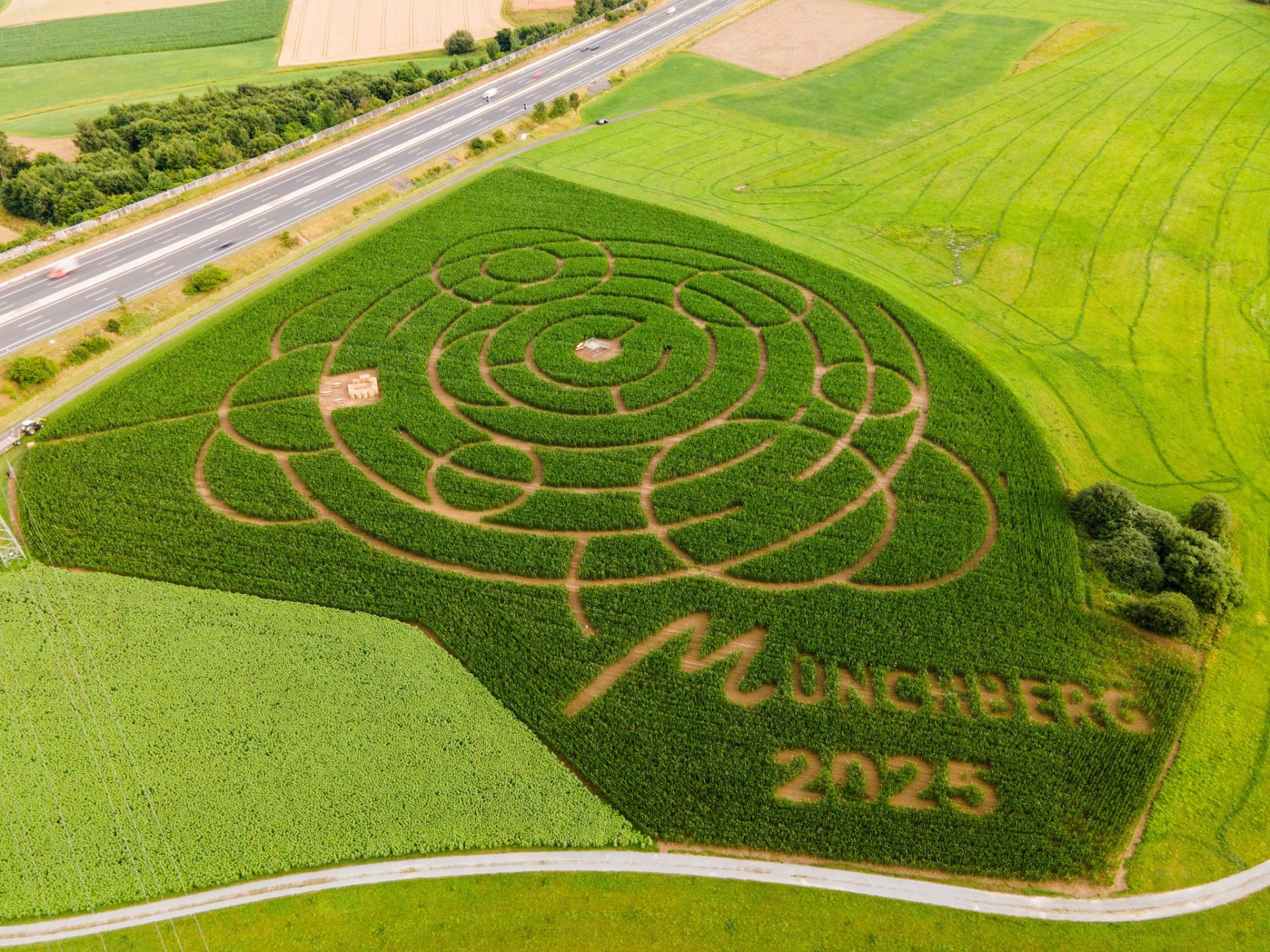Auf dem Bild sieht man ein Maislabyrinth von oben. Zusätzlich ist dort in den Mais Münchberg 2025 geschrieben.